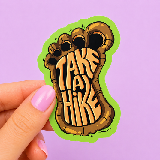 Sleazy Greetings funny die-cut vinyl sticker featuring a giant Bigfoot footprint with the phrase ‘Take a Hike’ carved into the sole. Cryptid-inspired outdoor humor sticker with rustic earthy tones, bold typography, and playful wilderness aesthetic.