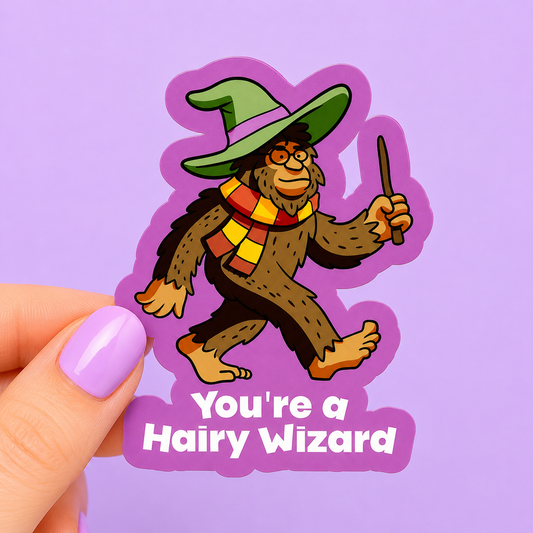Sleazy Greetings funny die-cut vinyl sticker featuring a Bigfoot dressed like a wizard with glasses, scarf, wand, and witch hat beside the phrase ‘You’re a Hairy Wizard.’ Cute cryptid parody sticker with magical fantasy humor and playful cartoon aesthetic.