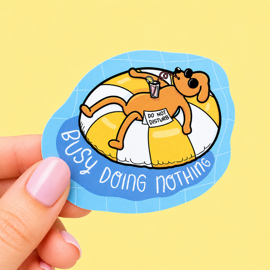 Sleazy Greetings funny die-cut vinyl sticker featuring a relaxed little dog floating in a pool tube beside the phrase ‘Busy Doing Nothing.’ Chaotic lazy-day sticker with playful vacation vibes, cute cartoon artwork, and aggressively unproductive gremlin energy.