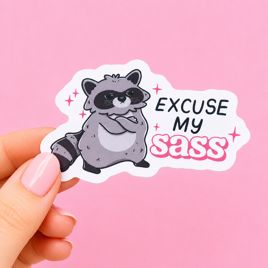 Sleazy Greetings funny die-cut vinyl sticker featuring a judgmental little raccoon beside the phrase ‘Excuse My Sass.’ Cute chaotic trash-animal sticker with sparkly pastel aesthetics, aggressively sassy energy, and unapologetic gremlin vibes.