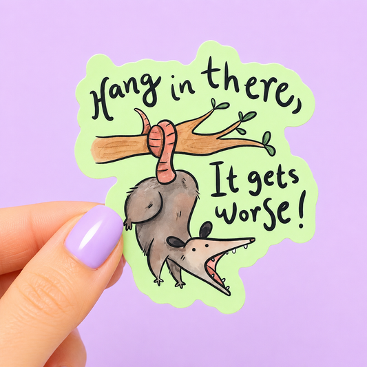 Sleazy Greetings funny die-cut vinyl sticker featuring an upside-down possum hanging from a tree branch beside the phrase ‘Hang in There, It Gets Worse!’ Cute chaotic possum sticker with sarcastic encouragement humor, whimsical watercolor-style artwork, and emotionally exhausted trash-animal energy.