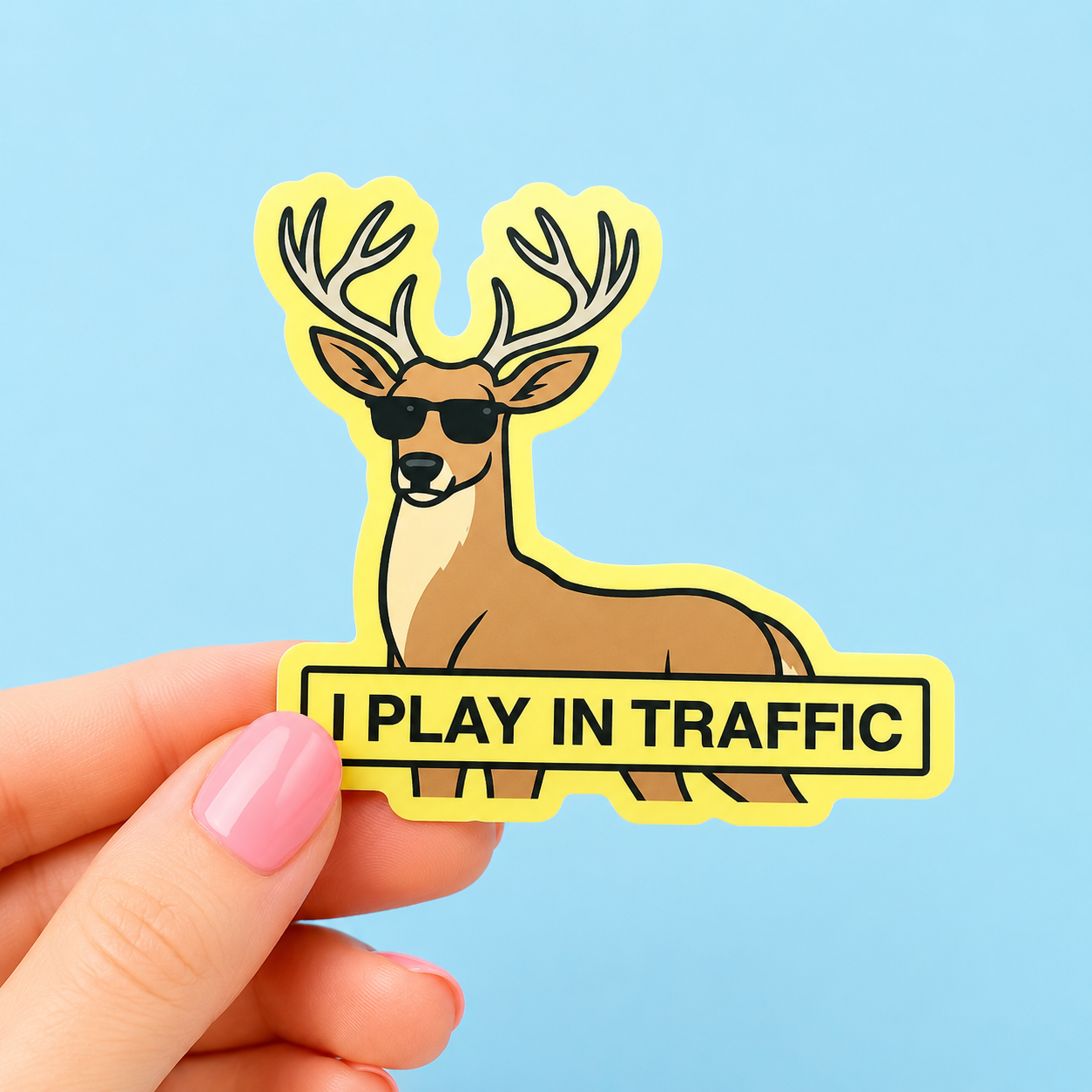 Sleazy Greetings funny die-cut vinyl sticker featuring a smug deer wearing sunglasses beside the phrase ‘I Play in Traffic.’ Chaotic woodland-animal sticker with reckless gremlin humor, playful cartoon artwork, and aggressively unbothered menace energy.