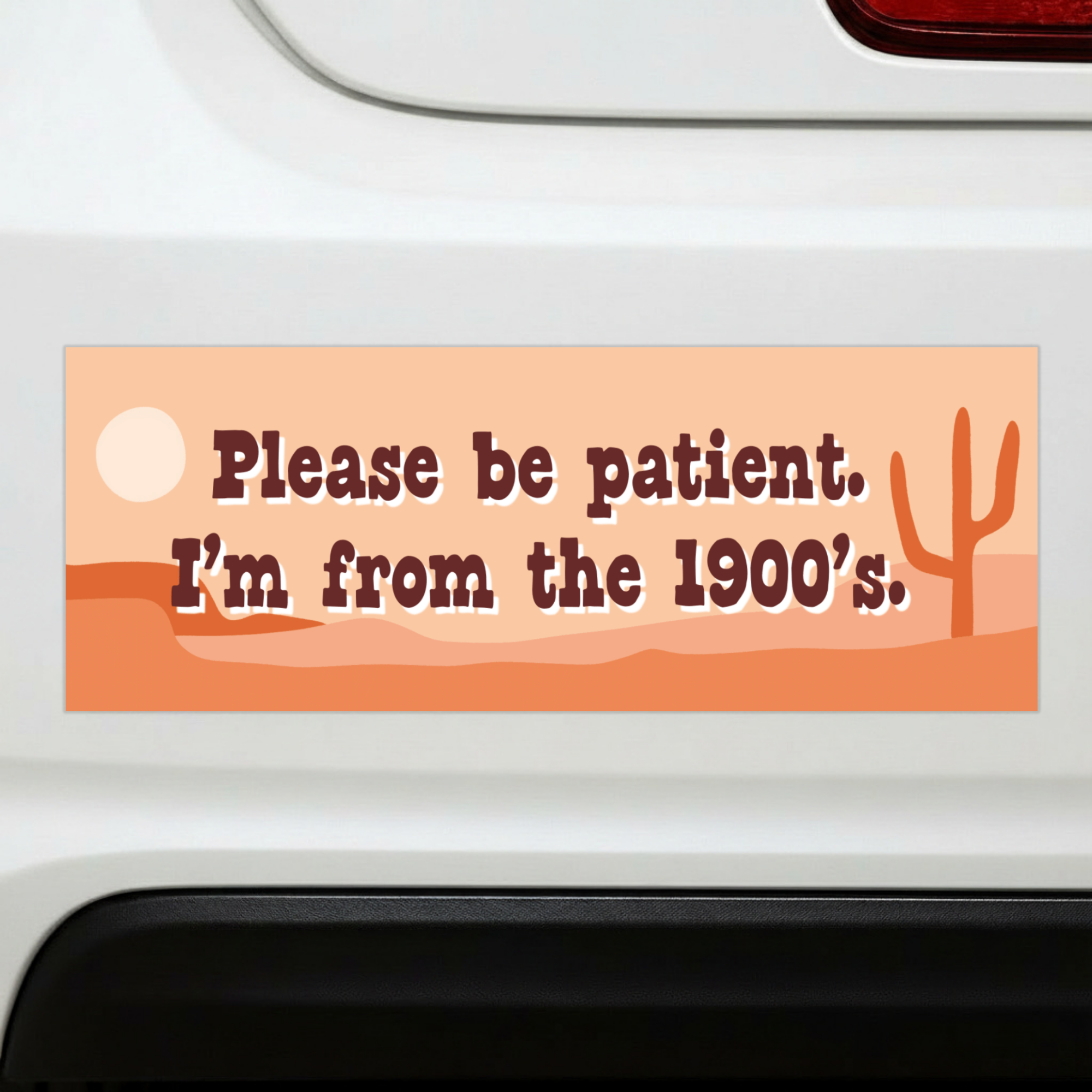 Sleazy Greetings funny bumper magnet displayed on the back of a white car featuring the phrase ‘Please Be Patient, I’m From The 1900’s.’ in retro brown typography on a warm desert-themed background with minimalist cactus and sunset illustrations. Humorous novelty car magnet with vintage-inspired aesthetic and generational humor shown in real-life automotive use.