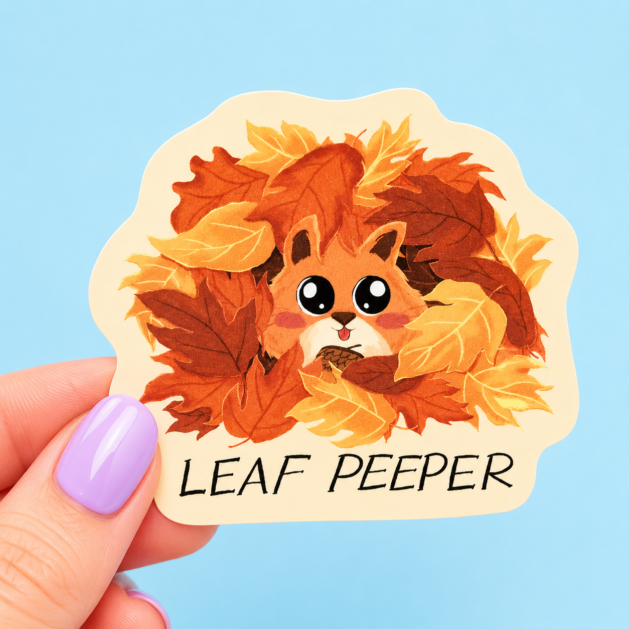 Sleazy Greetings cute die-cut vinyl sticker featuring an adorable fox peeking out from a pile of autumn leaves beside the phrase ‘Leaf Peeper.’ Cozy fall-themed sticker with cottagecore woodland vibes, playful seasonal humor, and soft whimsical artwork.