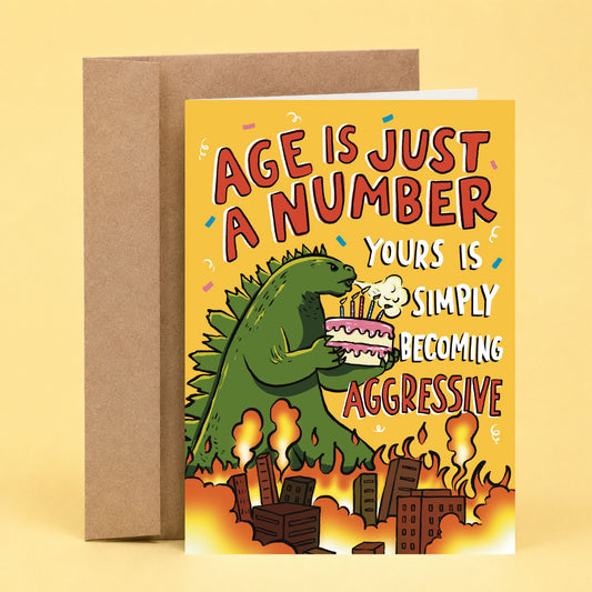 Sleazy Greetings funny birthday card featuring a Godzilla-style monster holding a birthday cake above a burning city, with the phrase, “Age Is Just a Number, Yours Is Simply Becoming Aggressive.” Hilarious aging humor card for friends, family, and anyone getting older.