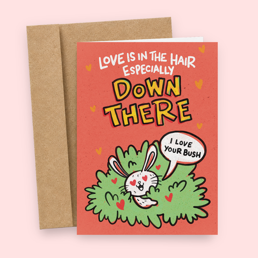 Sleazy Greetings funny Valentine's Day greeting card featuring a cute white bunny hiding in a green bush with pink hearts on a coral background with the phrase “Love Is in the Hair Especially Down There” and speech bubble “I Love Your Bush.” Naughty adult humor romantic card for couples, partners, and Valentine's Day.