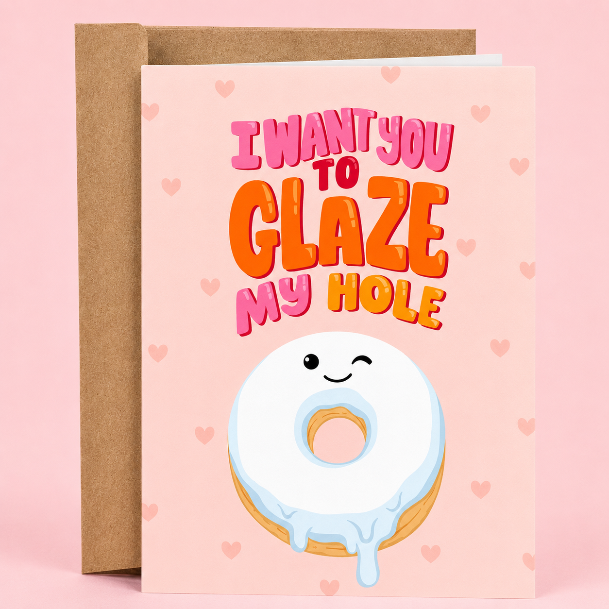 Sleazy Greetings funny romantic card featuring a smiling glazed donut on a soft pink background filled with tiny hearts. The card reads, “I Want You to Glaze My Hole,” making a playful donut-themed innuendo, and is displayed with a kraft envelope.