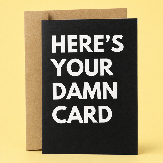 Sleazy Greetings funny minimalist greeting card featuring bold white typography on a solid black background that reads, “Here’s Your Damn Card.” A sarcastic and straightforward card perfect for birthdays, celebrations, or any occasion when you just need to hand over a card. Displayed with a kraft envelope against a soft yellow background.
