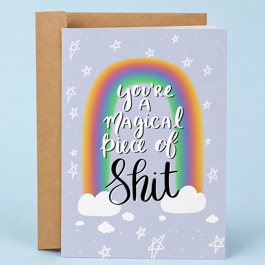 Sleazy Greetings funny friendship and love greeting card featuring a colorful rainbow, clouds, and hand-lettered typography with the sarcastic message “You’re a Magical Piece of Shit” on a pastel lavender background, displayed with a kraft envelope for a humorous birthday card, friendship card, encouragement card, anniversary card, or funny card for someone special.