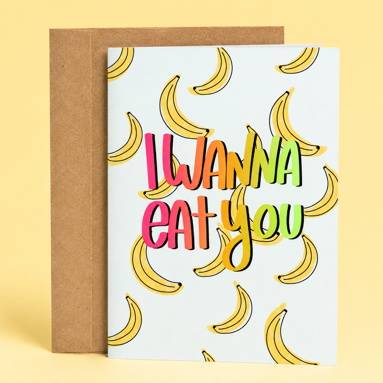 Sleazy Greetings funny adult love greeting card featuring a playful banana pattern and colorful hand-lettered typography reading “I Wanna Eat You,” displayed with a kraft envelope on a soft yellow background, perfect for Valentine’s Day, anniversaries, spouses, partners, boyfriends, girlfriends, husbands, and wives.