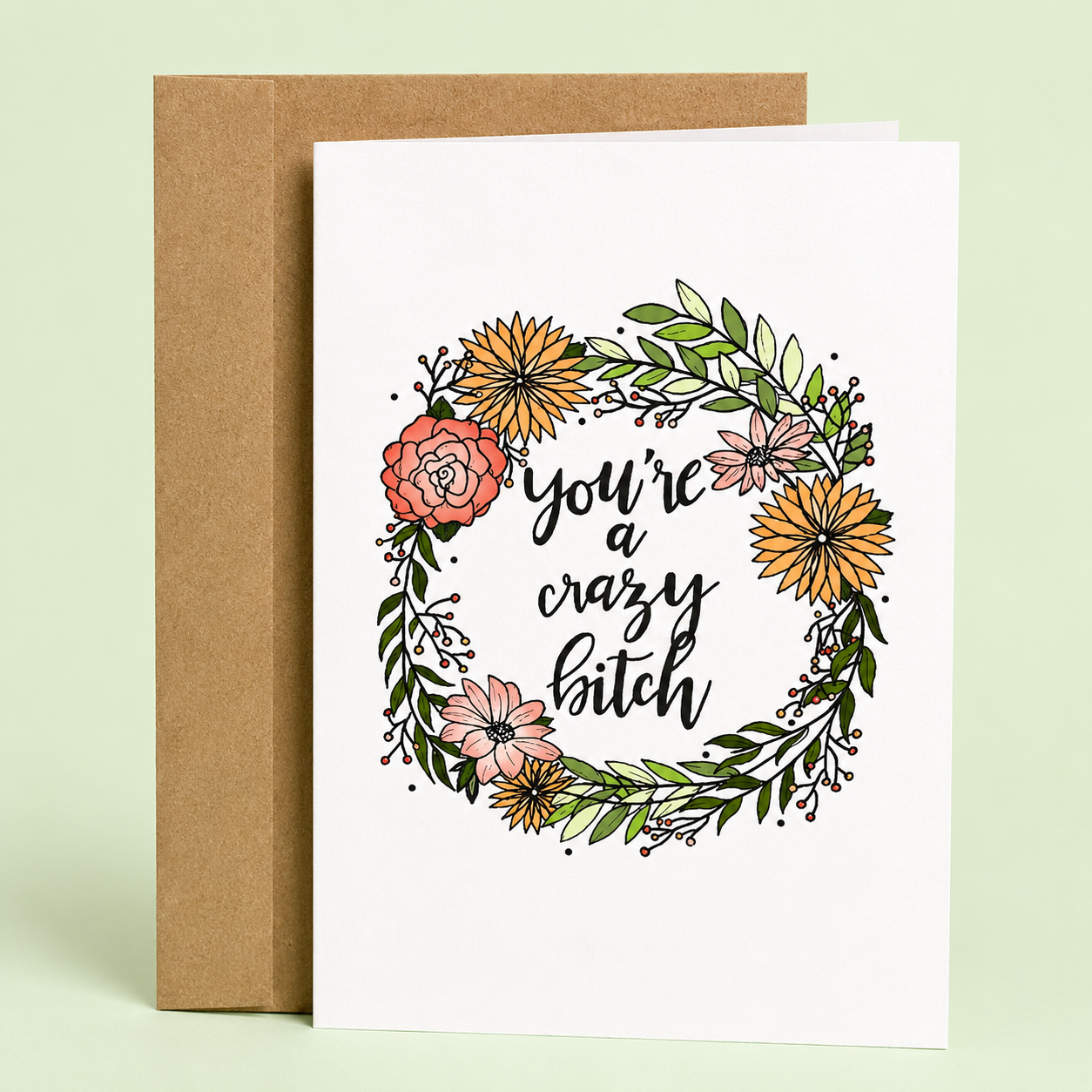 Sleazy Greetings funny friendship greeting card featuring a colorful floral wreath with hand-lettered typography reading “You’re a Crazy Bitch” on a white background, displayed with a kraft envelope for a humorous birthday card, best friend card, encouragement card, Galentine’s Day gift, or funny greeting card for someone who embraces their wild side.