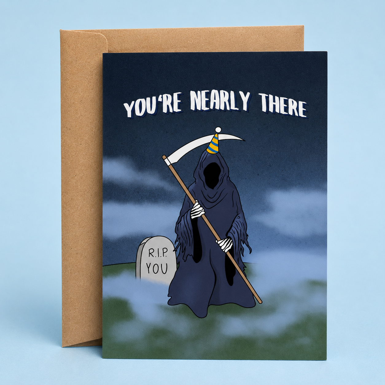 Sleazy Greetings funny birthday card featuring the Grim Reaper standing in a foggy graveyard while wearing a blue and yellow party hat. The card reads, “You’re Nearly There,” with a nearby tombstone humorously engraved “R.I.P. You,” creating a darkly funny joke about getting older. Displayed with a kraft envelope against a soft blue background, this sarcastic birthday card is perfect for friends, coworkers, siblings, parents, and anyone who appreciates morbid humor and aging jokes.