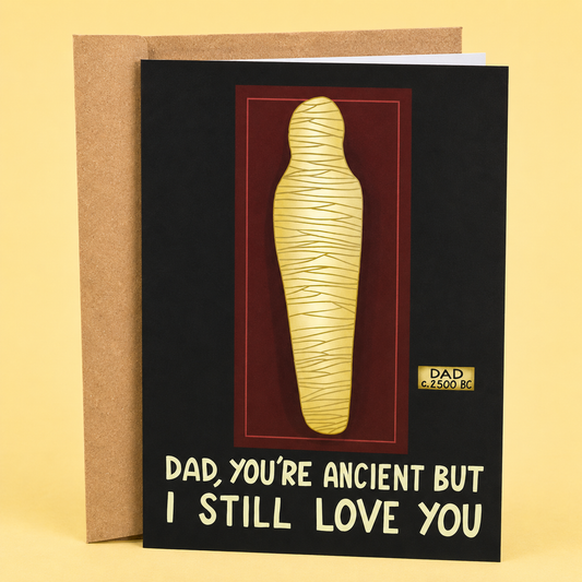 Sleazy Greetings funny Father’s Day greeting card featuring a mummy displayed in a museum exhibit with the sarcastic message “Dad, You’re Ancient But I Still Love You,” on a black background, displayed with a kraft envelope for a humorous Father’s Day card.