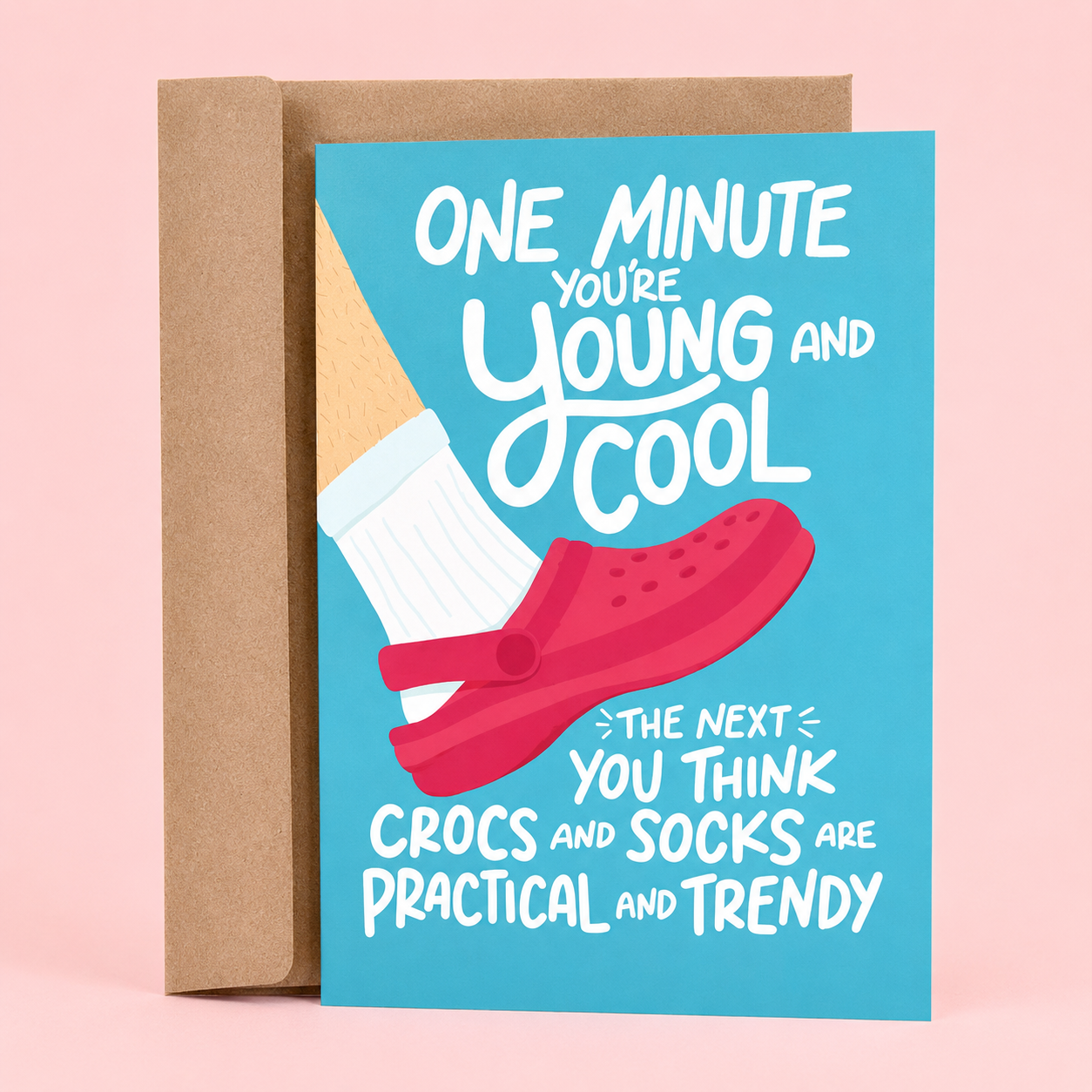 Sleazy Greetings funny birthday card featuring a person wearing white socks and bright pink Crocs on a blue background, with the age-related joke “One Minute You’re Young and Cool, The Next You Think Crocs and Socks Are Practical and Trendy,” paired with a kraft envelope.