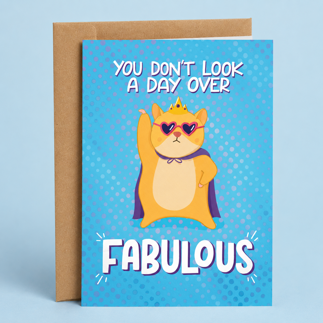 Sleazy Greetings funny birthday card featuring a confident orange cat wearing a crown, cape, and heart-shaped sunglasses on a bright blue comic-style background, with the compliment “You Don’t Look a Day Over Fabulous,” paired with a kraft envelope.