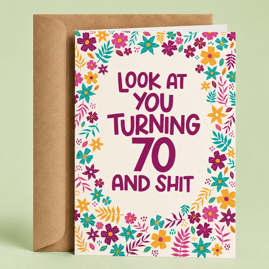Sleazy Greetings funny 70th birthday card featuring a colorful floral border with bright pink, purple, teal, and yellow flowers on a cream background, with the playful message “Look At You Turning 70 And Shit,” paired with a kraft envelope.