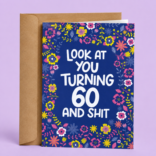 Sleazy Greetings funny 60th birthday card featuring a vibrant floral border with pink, yellow, and purple flowers on a blue background, with the playful message “Look At You Turning 60 And Shit,” paired with a kraft envelope.