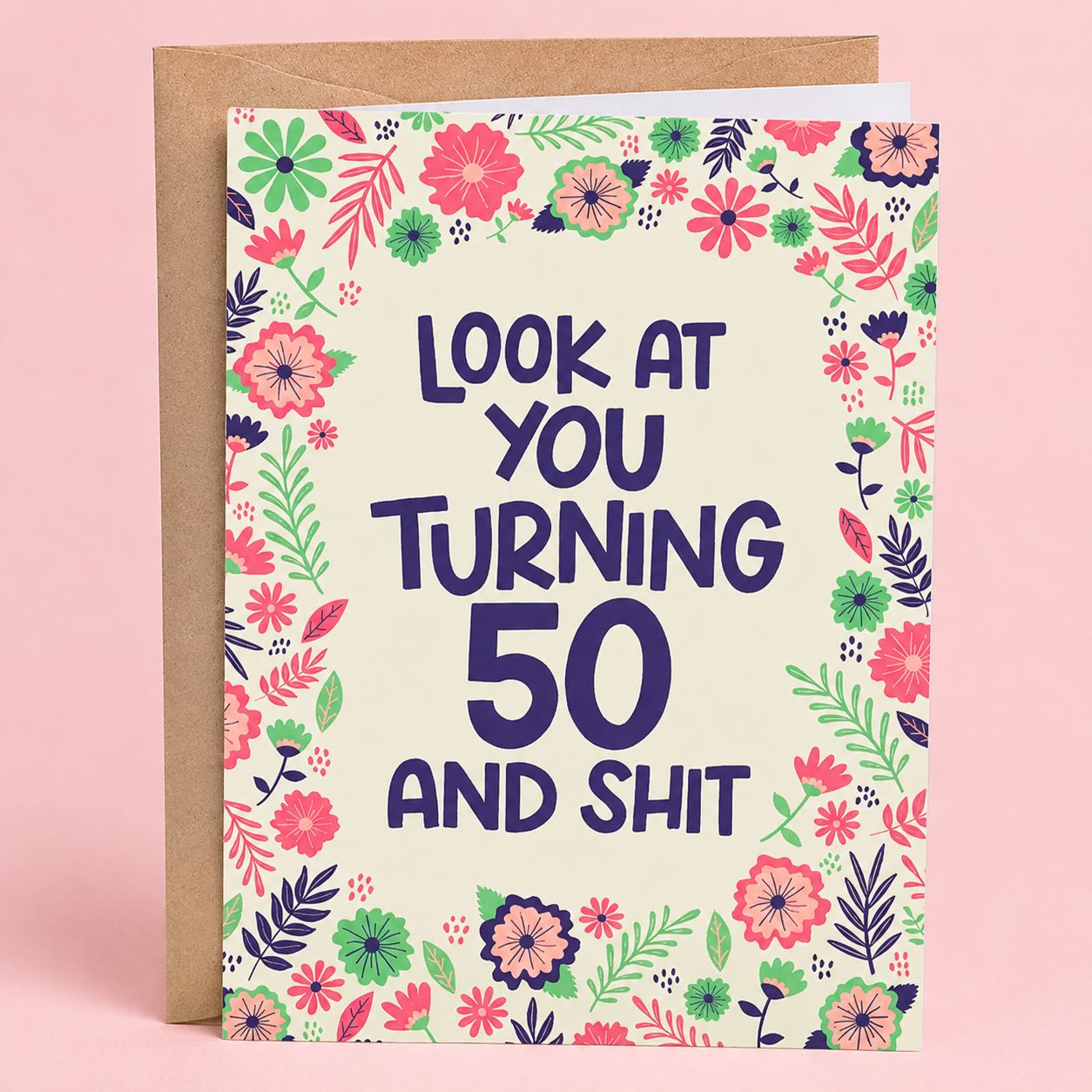 Sleazy Greetings funny 50th birthday card featuring a colorful floral border with pink, purple, and green flowers on a cream background, with the playful message “Look At You Turning 50 And Shit,” paired with a kraft envelope.