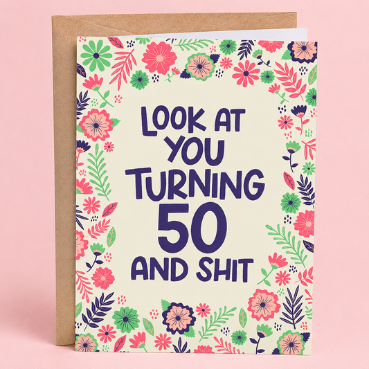Sleazy Greetings funny 50th birthday card featuring a colorful floral border with pink, purple, and green flowers on a cream background, with the playful message “Look At You Turning 50 And Shit,” paired with a kraft envelope.