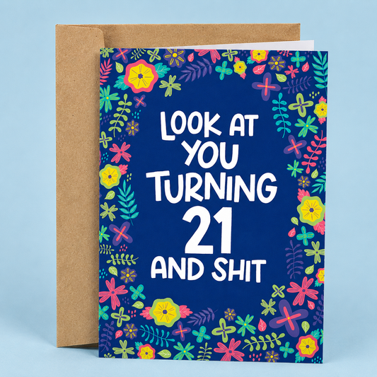 Sleazy Greetings funny 21st birthday card featuring a bright floral border with colorful flowers and greenery on a dark blue background, with the playful message “Look At You Turning 21 And Shit,” paired with a kraft envelope.