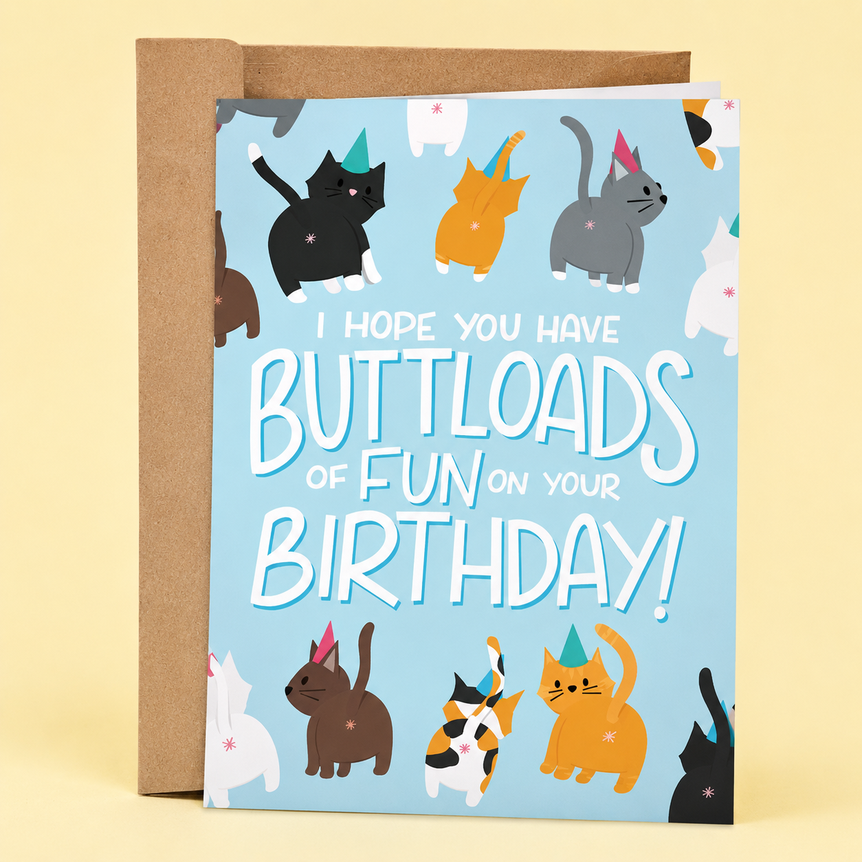 Sleazy Greetings funny birthday card featuring colorful cartoon cats showing their backsides while wearing party hats on a light blue background, with the pun-filled message “I Hope You Have Buttloads of Fun on Your Birthday!” paired with a kraft envelope.