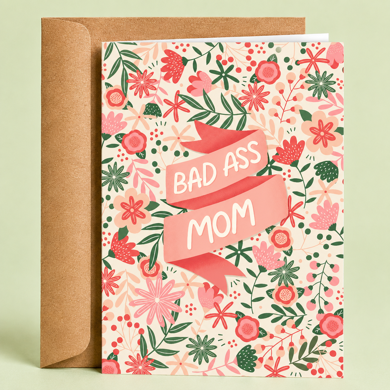 Sleazy Greetings funny Mother’s Day card featuring a pink floral pattern filled with flowers and greenery, with a ribbon banner across the center that reads “Bad Ass Mom,” paired with a kraft envelope.