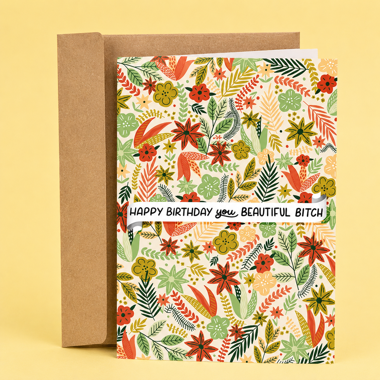 Sleazy Greetings funny birthday card featuring a colorful floral pattern filled with illustrated flowers and leaves, with a banner across the center that reads “Happy Birthday You Beautiful Bitch,” paired with a kraft envelope.