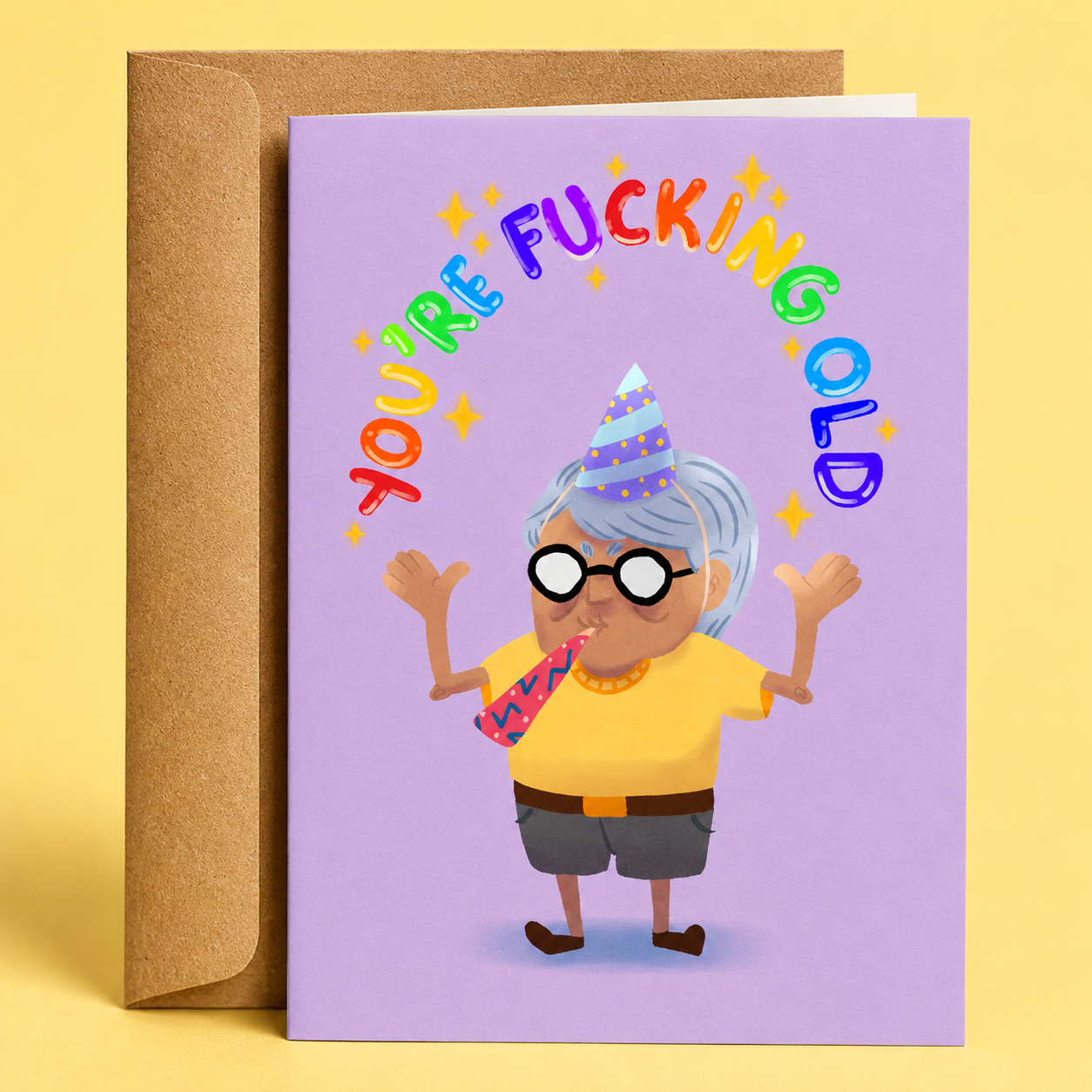 Sleazy Greetings funny birthday card featuring a partying grandma wearing a birthday hat and blowing a party horn on a purple background with rainbow lettering that reads “You’re Fucking Old,” paired with a kraft envelope.