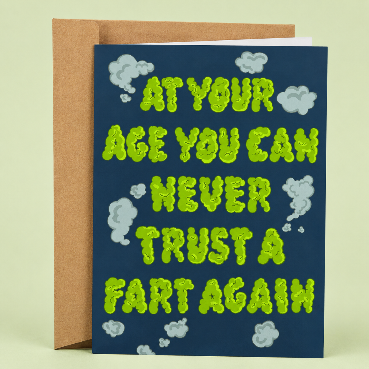 Sleazy Greetings funny trust and friendship card featuring green fart-cloud lettering and puffs of gas on a dark blue background with the message “At Your Age You Can Never Trust A Fart Again,” paired with a kraft envelope.