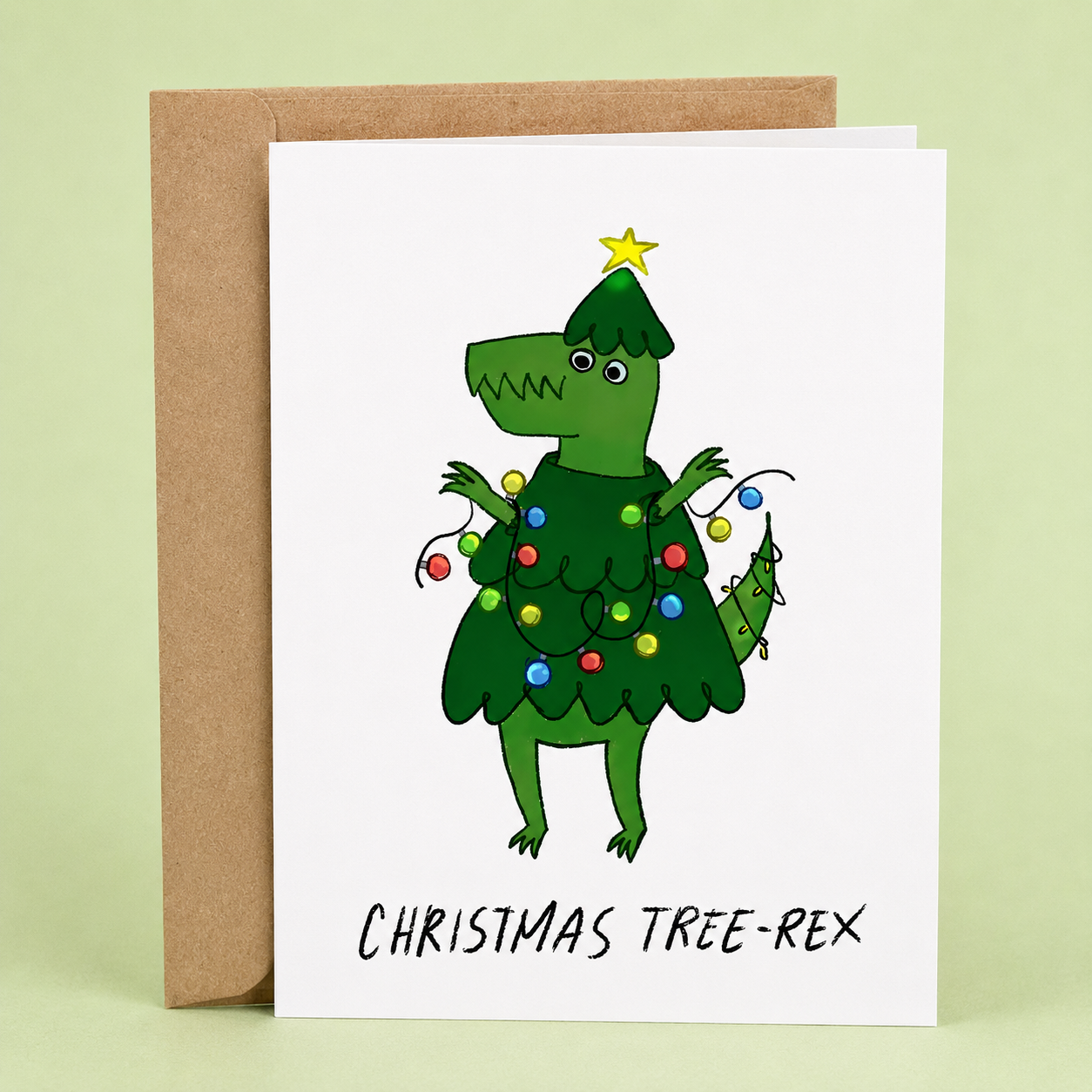 Sleazy Greetings funny Christmas greeting card featuring a dinosaur dressed as a Christmas tree and wrapped in colorful holiday lights with the pun “Christmas Tree-Rex,” paired with a kraft envelope.