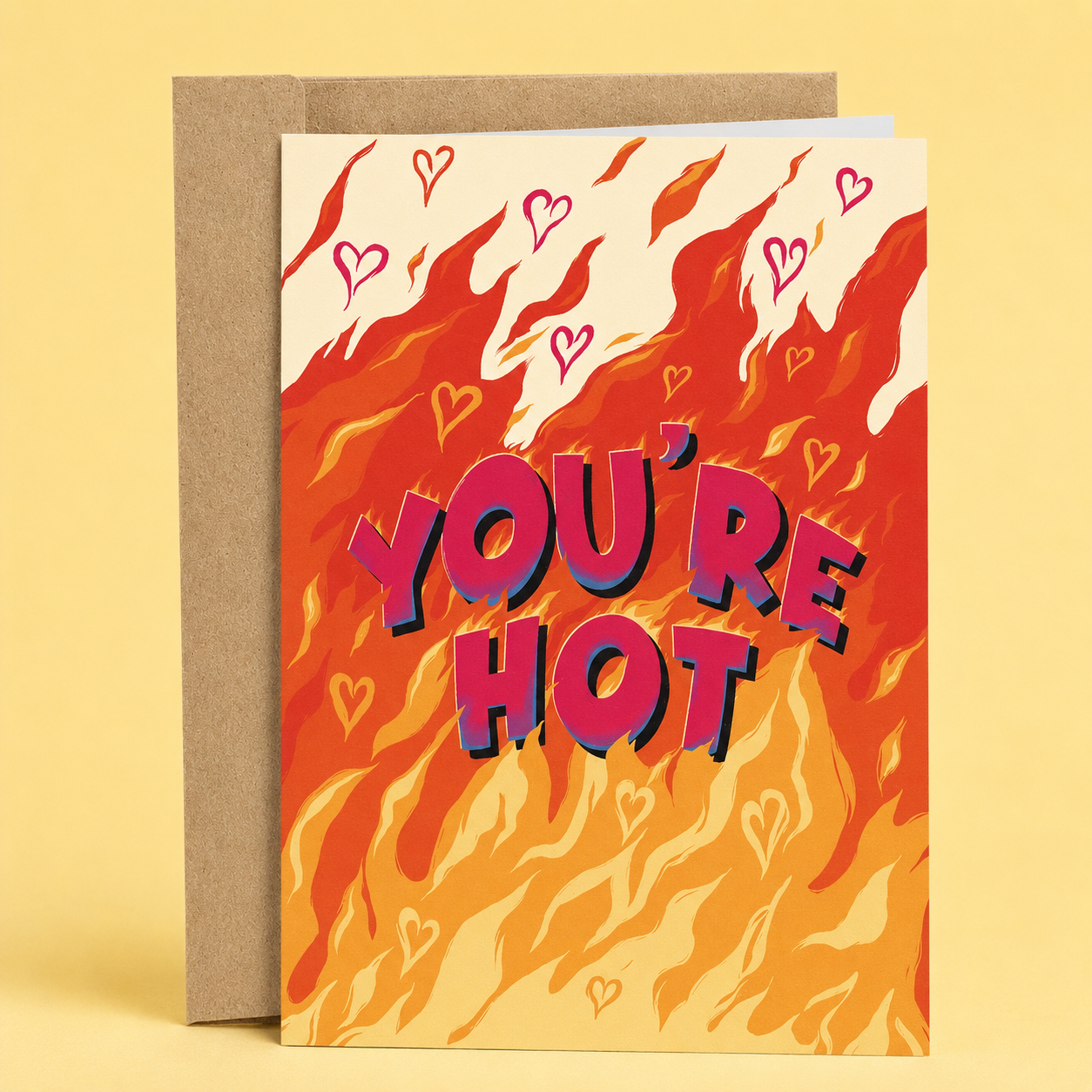 A greeting card with a colorful front design featuring the text 'You're Hot' surrounded by flames and hearts, presented against a beige background.