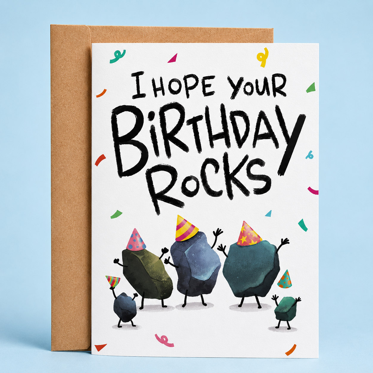 Sleazy Greetings funny birthday card featuring the phrase ‘I Hope Your Birthday Rocks!’ in bold hand-lettered typography above watercolor-style cartoon rocks wearing party hats. Playful pun birthday greeting card with colorful confetti accents and a kraft envelope included.