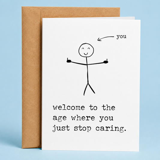 “Sleazy Greetings funny birthday card featuring a minimalist stick figure giving two middle fingers with an arrow labeled ‘you’ and the sarcastic message ‘welcome to the age where you just stop caring.’ Displayed as a premium white folded Sleazy Greetings card with kraft envelope.